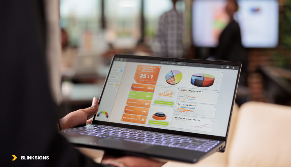 a laptop showing data dashboard and in background there is blurry screen with same dashboard data and two persons.