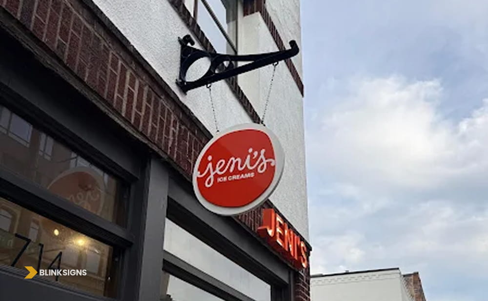 Round red Jeni's Ice Creams blade sign hanging from a brick storefront.